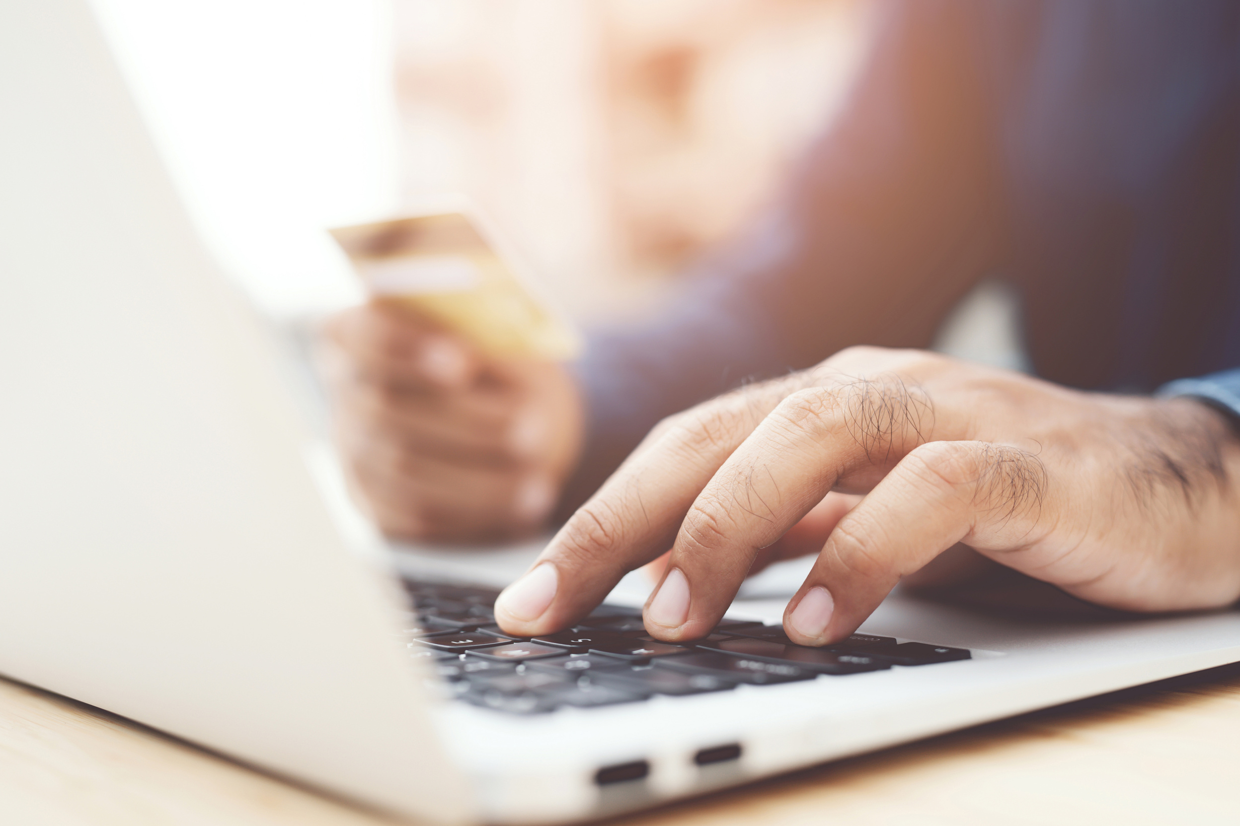 Hand Holding Bank Card and Typing on a Laptop Keyboard